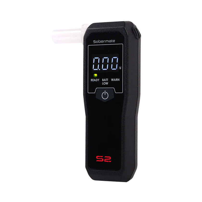 Tiny matte-black Sobermate S2 breathalyser next to a standard credit card for scale; device features a bright colour OLED screen showing “0.00” result, single button, and fold-out blow tube mouthpiece.